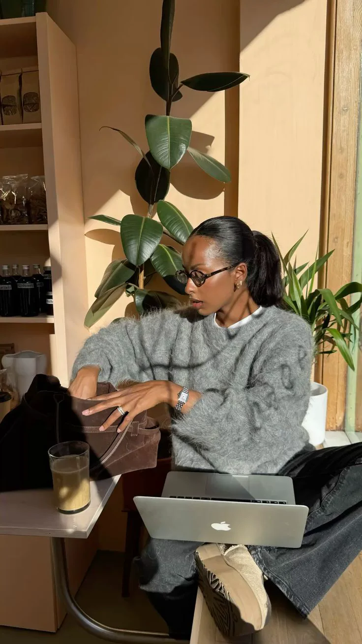A woman pauses in warm cafe light with a closed MacBook on her lap