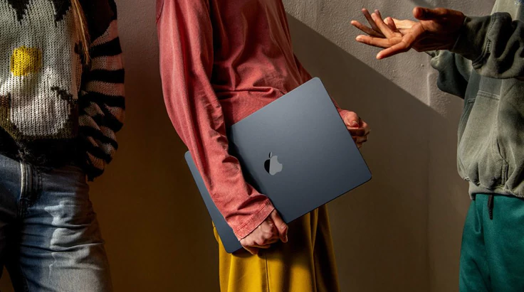 Three collaborators pause in warm studio light beside a closed MacBook