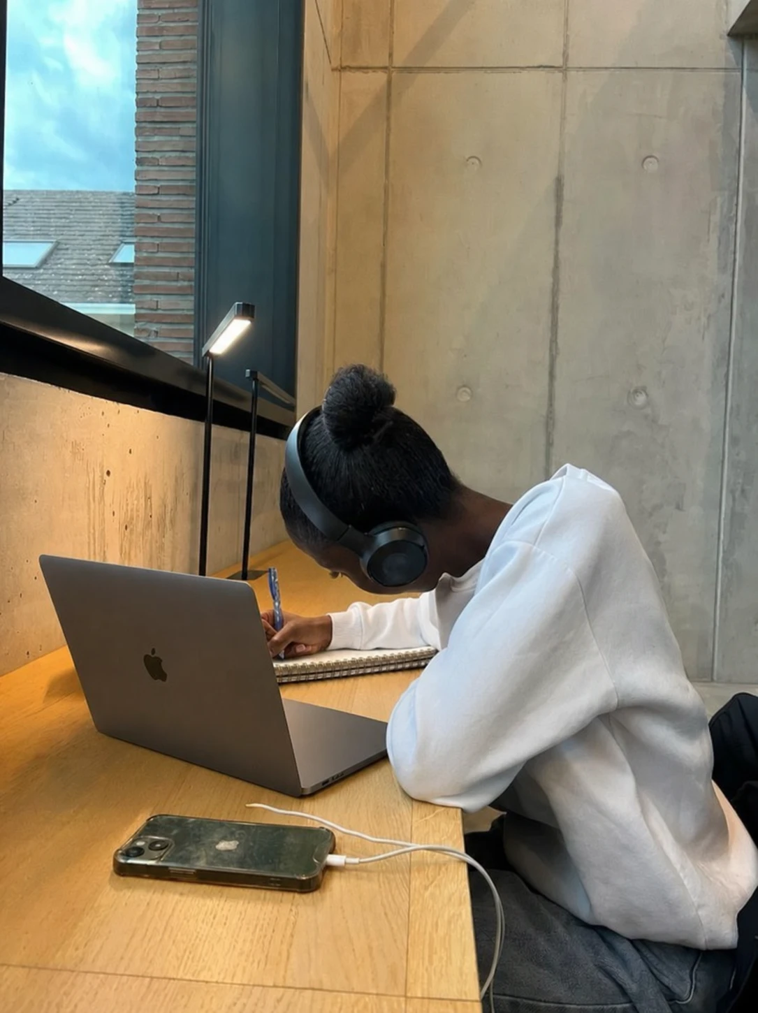 A student writes in a notebook beside a MacBook with its screen turned away